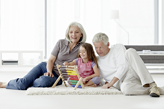 Pensioners playing with grandchild on white carpet.